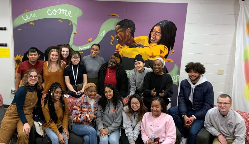 Group of MLC residents pose for a photo in front of a mural