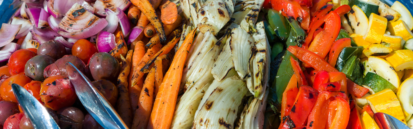 A mix of colorful grilled vegetables with metal serving tongs