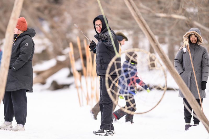 Undergraduate Kane Funmaker, Ho-Chunk bear clan member, prepares to throw a lance at a swinging hoop in the dakobijigan-minawaa zhiimaagan game while his partner, graduate student Shiqi Shen, looks on at the Ojibwe Winter Games on Lake Mendota