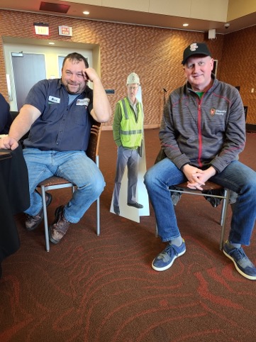 Two Facilities staff sitting for a group photo in front of a cutout
