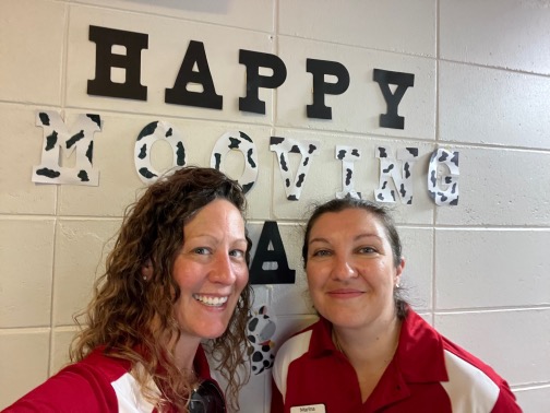 Two HR staff smiling for a photo in front of words "Happy Mooving Day" on a wall
