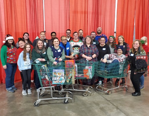 Staff posing for a group photo in holiday apparel with shopping carts filled with items