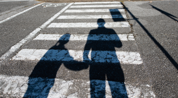 A shadow of an adult and child over a crosswalk on a road