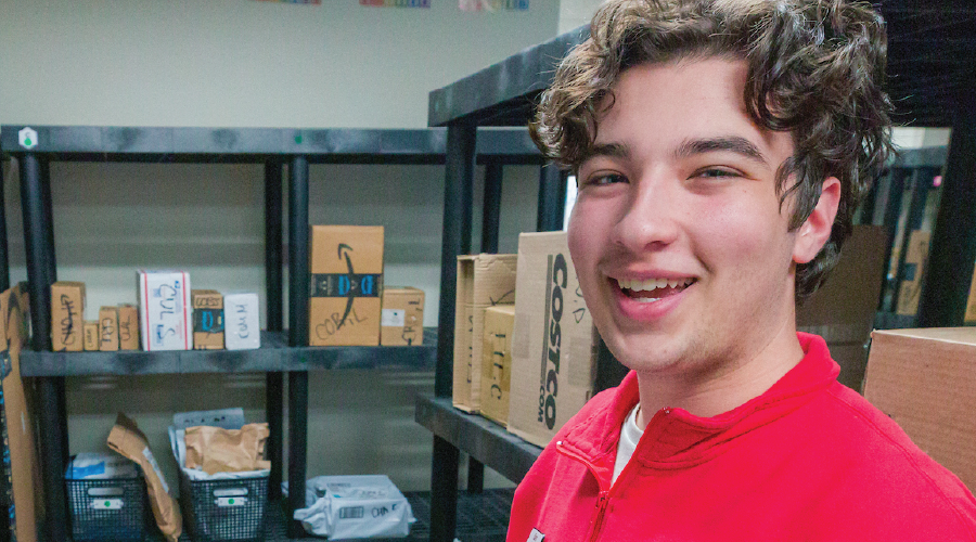 A Housing staff member smiles for a photo among packages on shelves