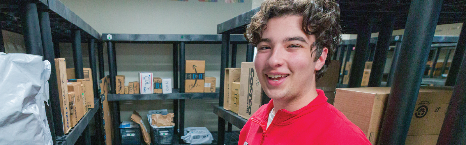 A Housing staff member smiles for a photo among packages on shelves