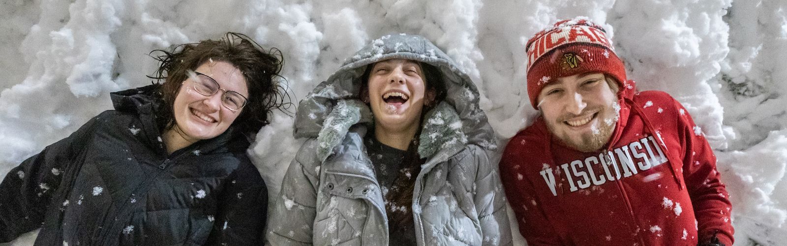 Undergraduate students Jenna Crolla (left), Liv Baumann (center), and Nick Mugnai (right) lie in the snow on Bascom Hill during a winter night snowfall at the University of Wisconsin–Madison on Dec. 15, 2022. (Photo by Taylor Wolfram / UW–Madison)