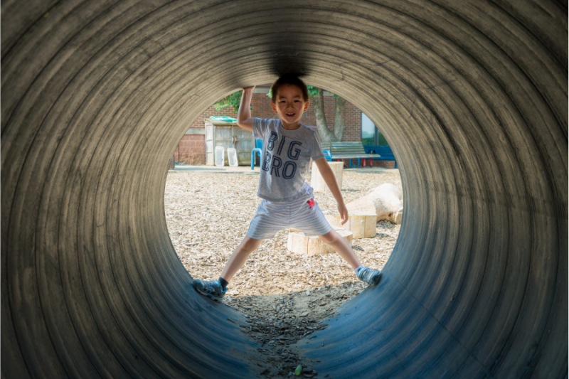 Little boy running through play tunnel at Eagle Heights outdoor recreation area.